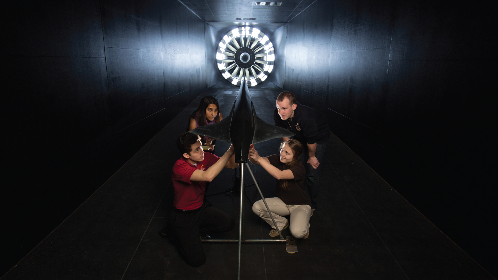 Four students fixing model plane in a wind tunnel with a glowing fan at the end